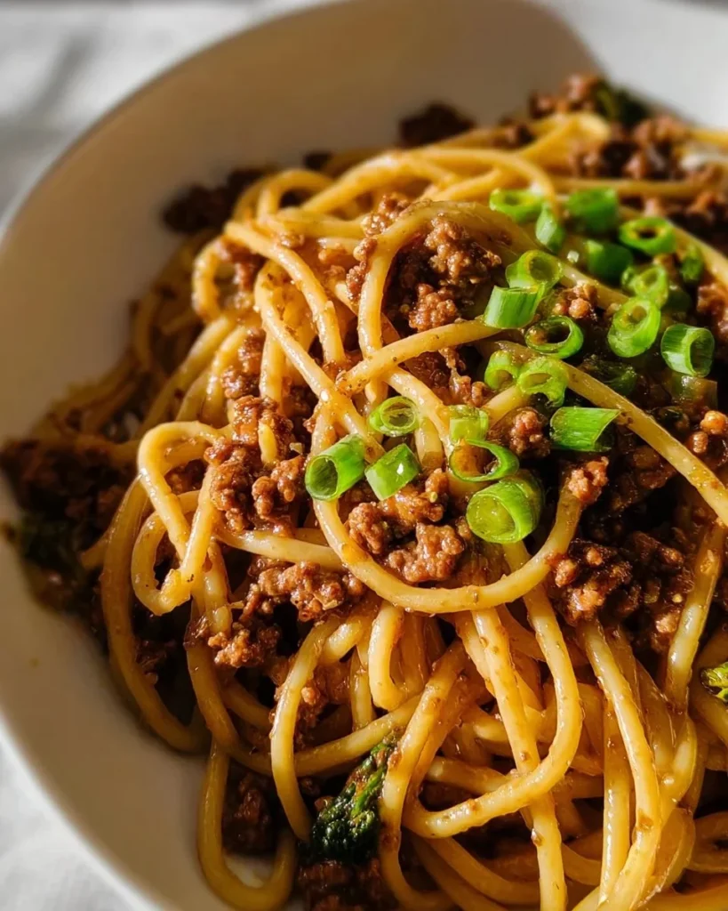Plate of Mongolian ground beef noodles garnished with green onions and sesame seeds