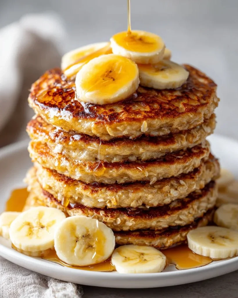 Stack of healthy banana oatmeal pancakes topped with fresh banana slices and syrup