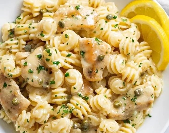 Plate of Chicken Piccata Pasta garnished with parsley and lemon slices