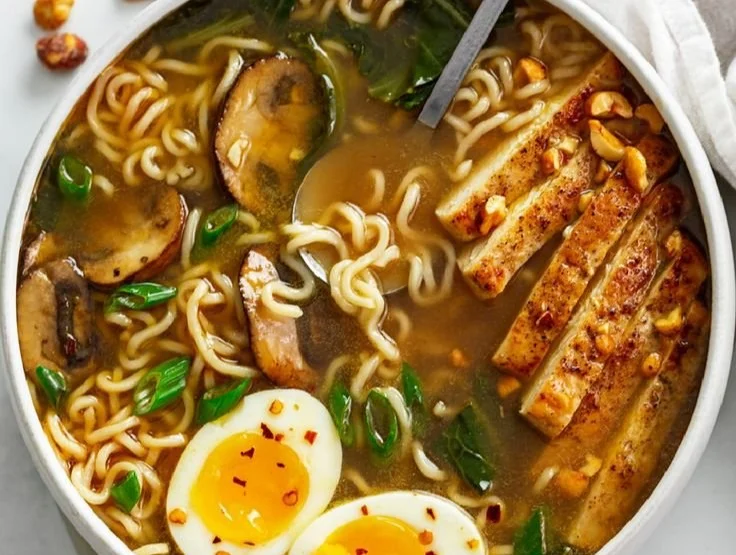 A bowl of steaming homemade ramen with toppings like egg, green onions, and pork.