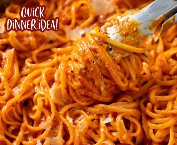 Dish of roasted red pepper pasta topped with fresh basil and parmesan cheese.