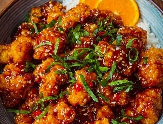 Crispy orange chicken drizzled with zesty sauce garnished with green onions.