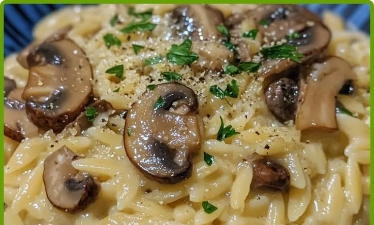 Bowl of creamy lemon mushroom orzo topped with fresh herbs and mushrooms.