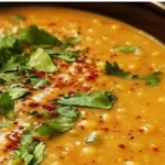 Bowl of easy spiced red lentil coconut soup garnished with herbs