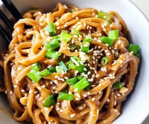 Bowl of quick and creamy peanut sauce rice noodles with fresh herbs and vegetables.