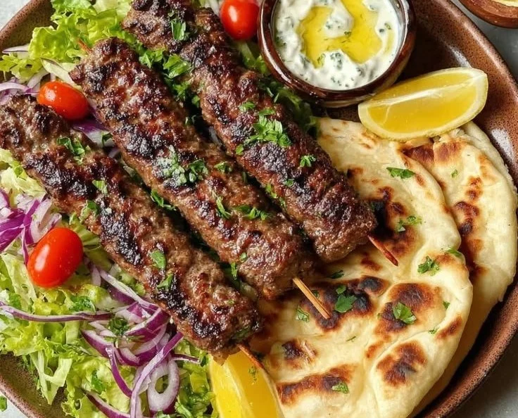 Plate of Middle Eastern Kafta Kebabs served with fresh herbs and sauces.
