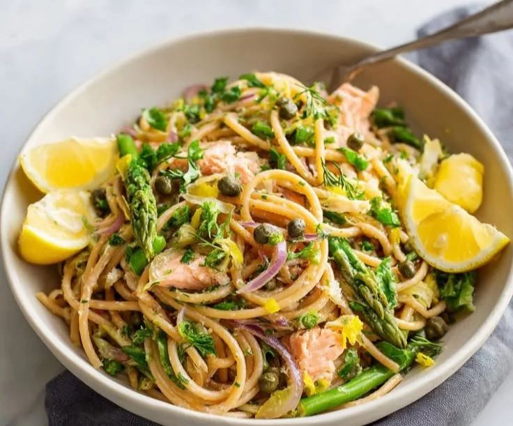 A serving of lemony salmon pasta with fresh herbs garnished on top.