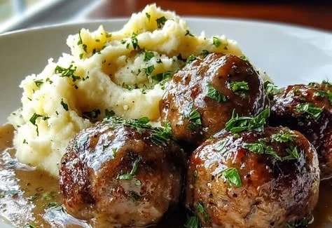 Salisbury steak meatballs served with garlic herb mashed potatoes on a plate.