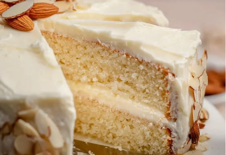 A slice of sweet almond cream cake garnished with almonds and fresh cream.